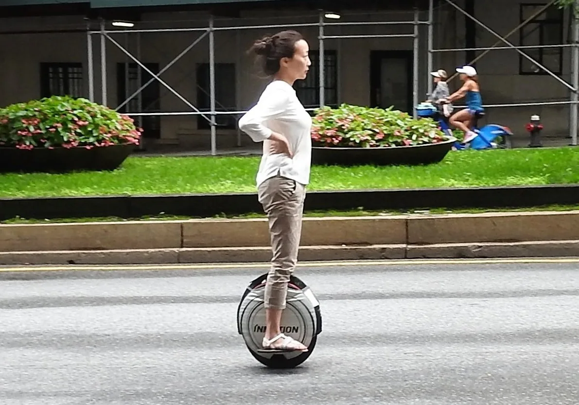 Personne debout sur une gyroroue électrique roulant sur une chaussée, vue de profil