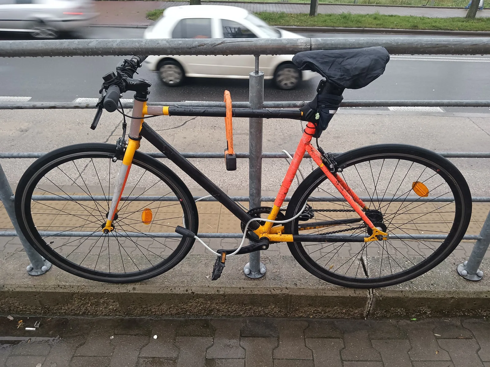 Vélo de ville attaché à une barrière par un antivol en U et un câble en acier sur un trottoir