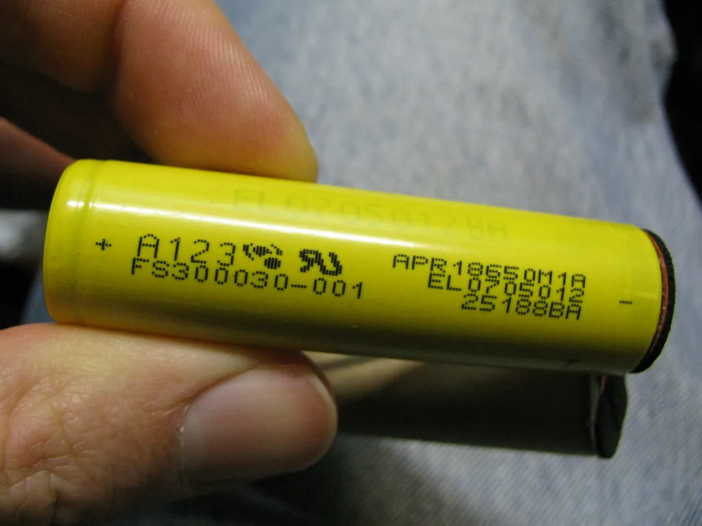 Cellule lithium-ion cylindrique jaune tenue entre les doigts, illustrant les éléments d'une batterie