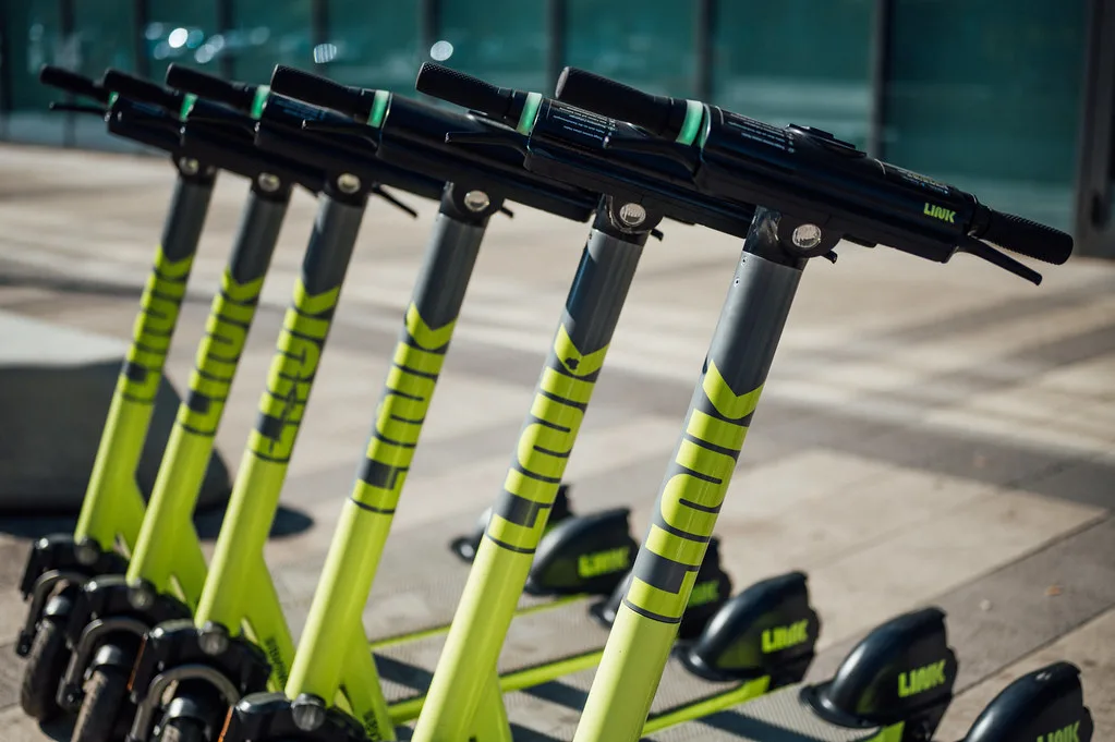 Rangée de trottinettes électriques vert fluo alignées sur un trottoir en ville