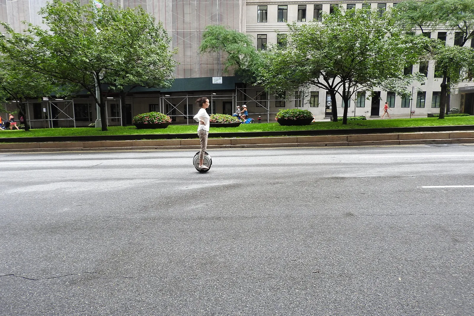 Rider de gyroroue roulant seul sur une large avenue urbaine bordée d'arbres