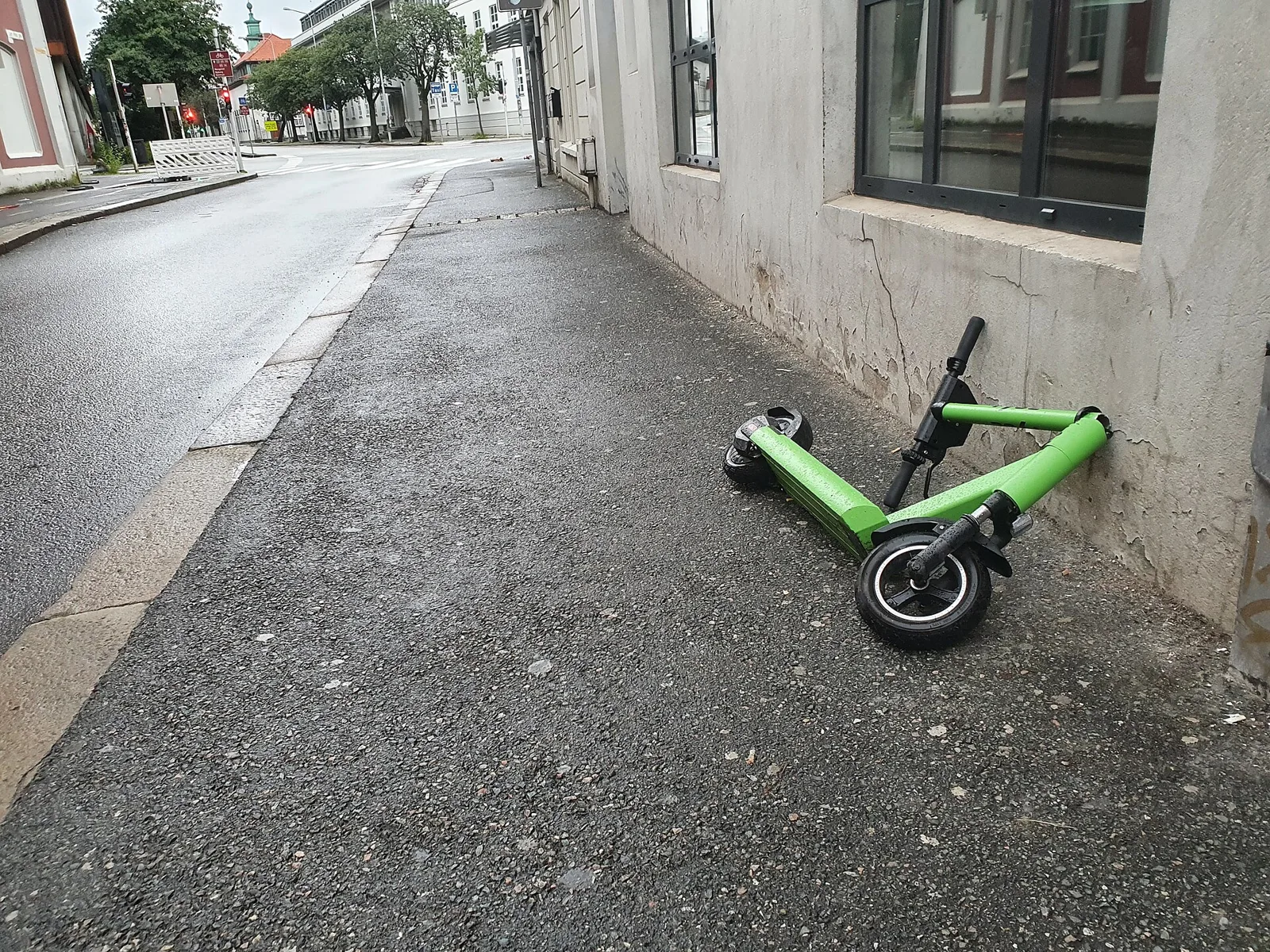 Trottinette électrique verte renversée sur un trottoir, le long d'un mur
