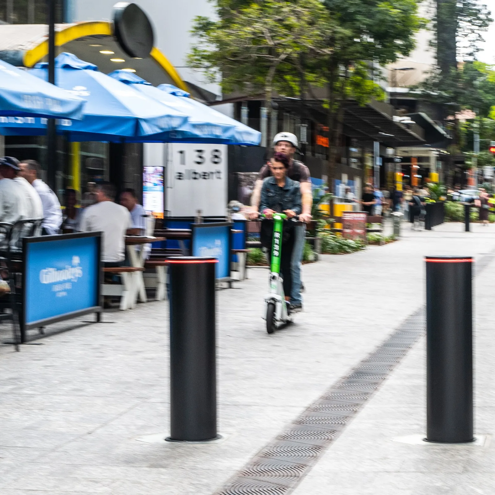 Utilisateur de trottinette électrique roulant sur un boulevard piéton entre des bornes et des terrasses