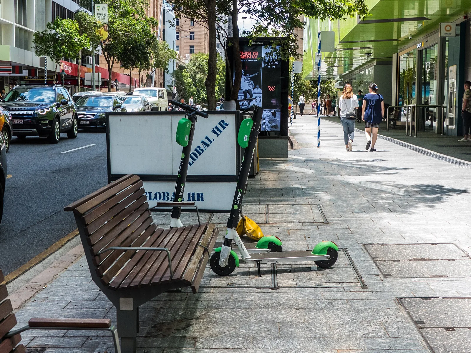 Trottinettes électriques garées sur un trottoir urbain près d'un banc en bois, rue ensoleillée