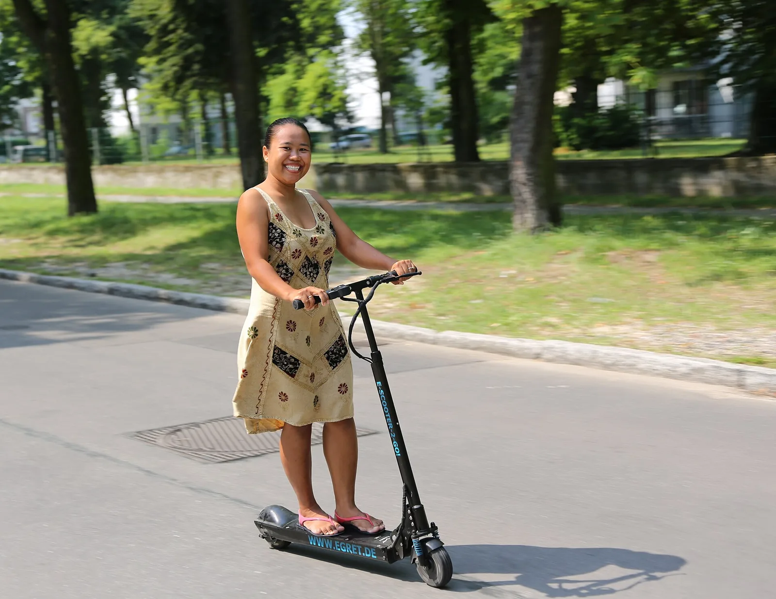 Femme souriante debout sur une trottinette électrique noire dans une allée arborée