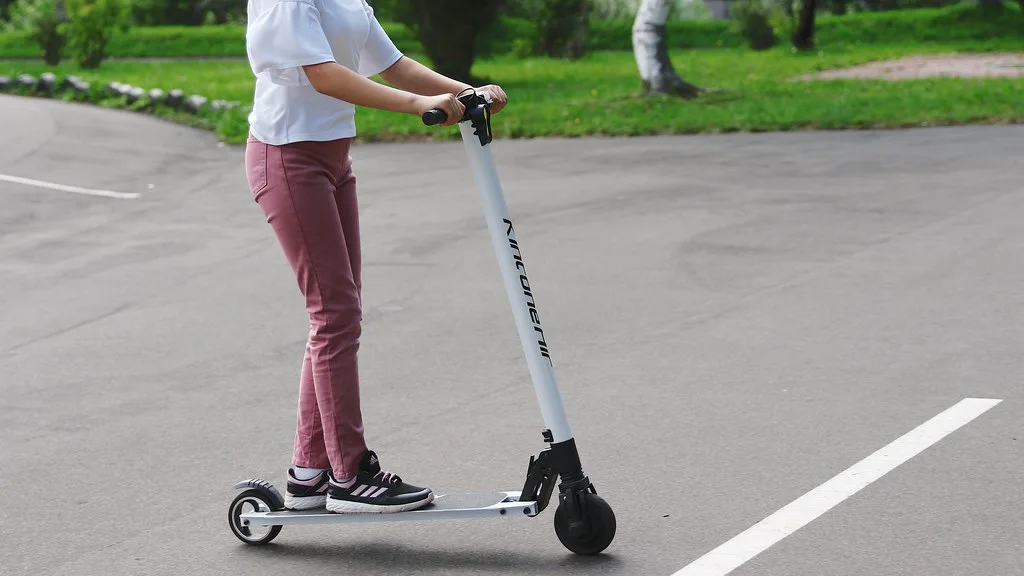 Personne debout sur une trottinette électrique légère blanche sur une allée goudronnée dans un parc