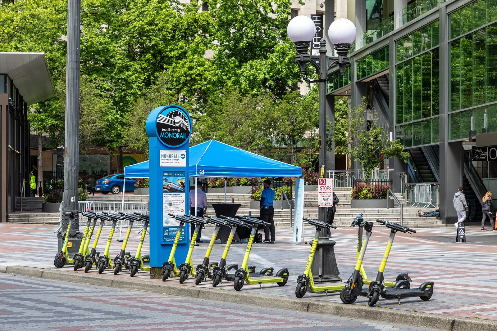 Trottinettes électriques alignées sur une place de ville entre immeubles et arbres verdoyants
